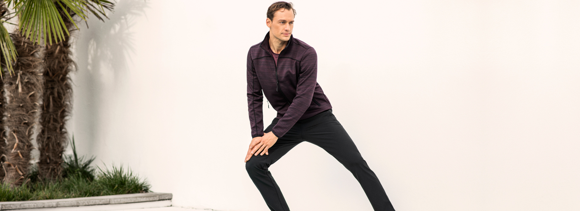 Mann in roter Sweatjacke und dunkler Hose der Marke JOY sportswear in sportlicher Pose.