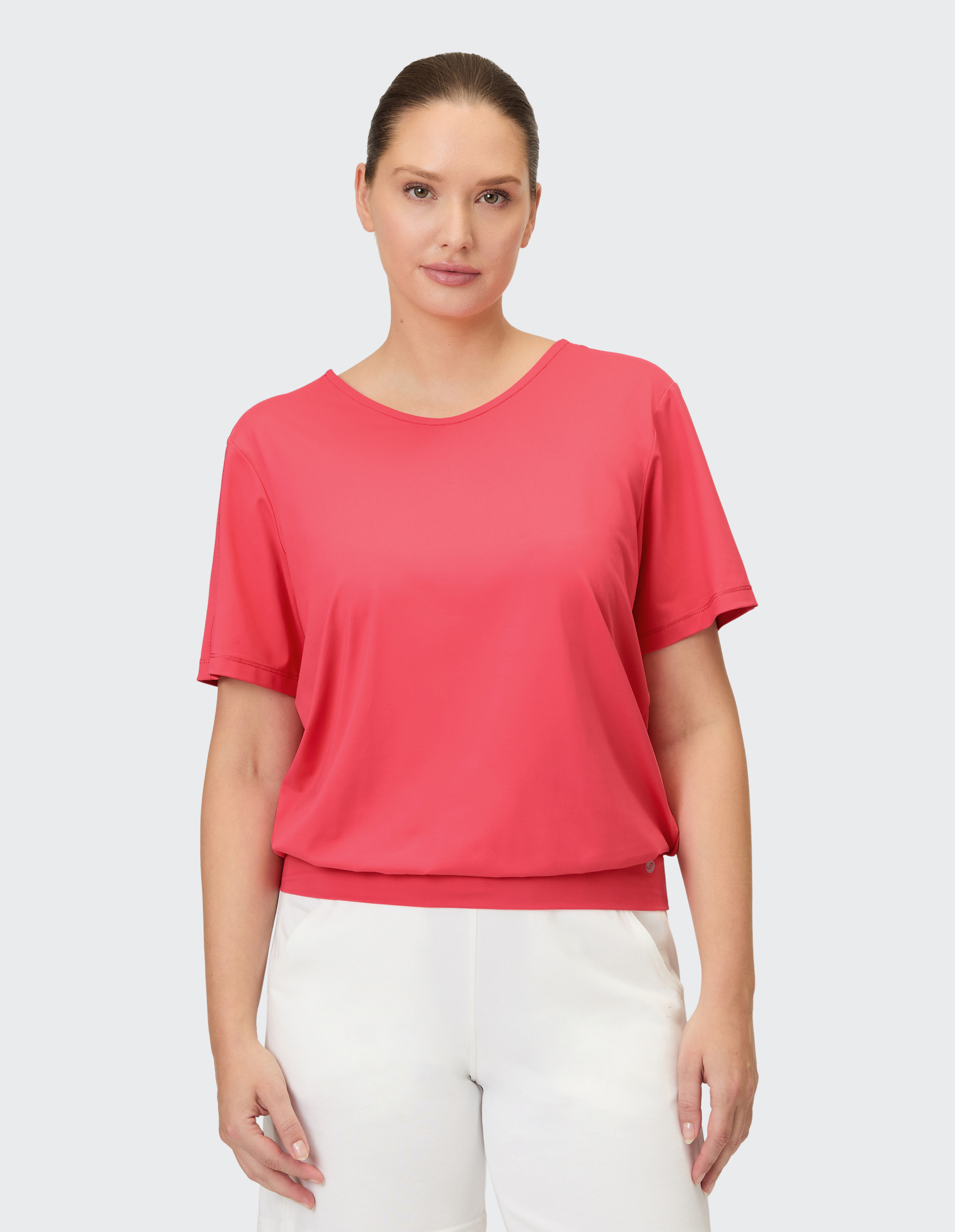 Eine Frau trägt ein korallenrotes T-Shirt mit V-Ausschnitt und elastischem Saum.