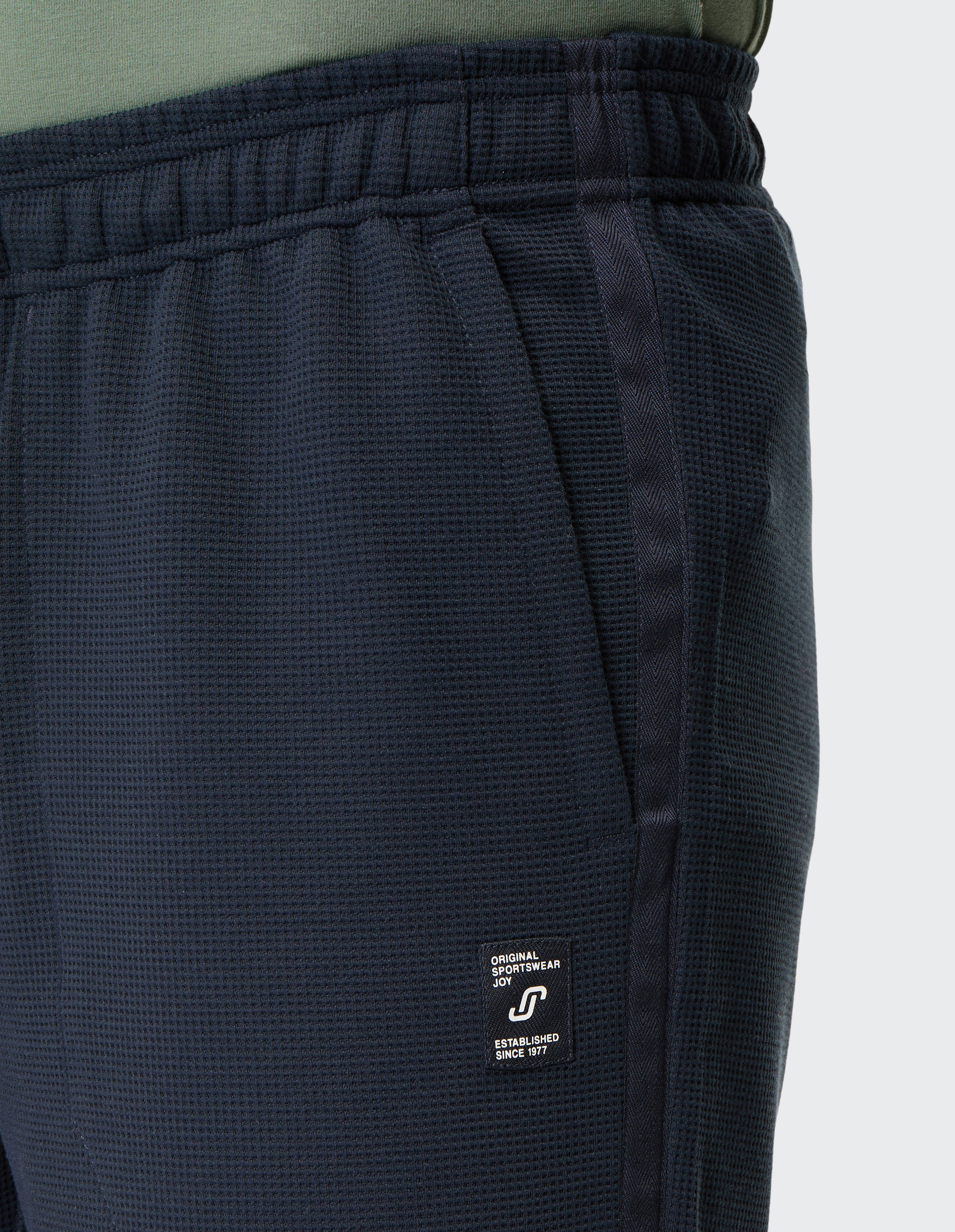 Dunkelblaue Sporthose mit Waffelmuster und elastischem Bund, Detailansicht auf das weiße Markenlabel nahe der rechten Tasche.