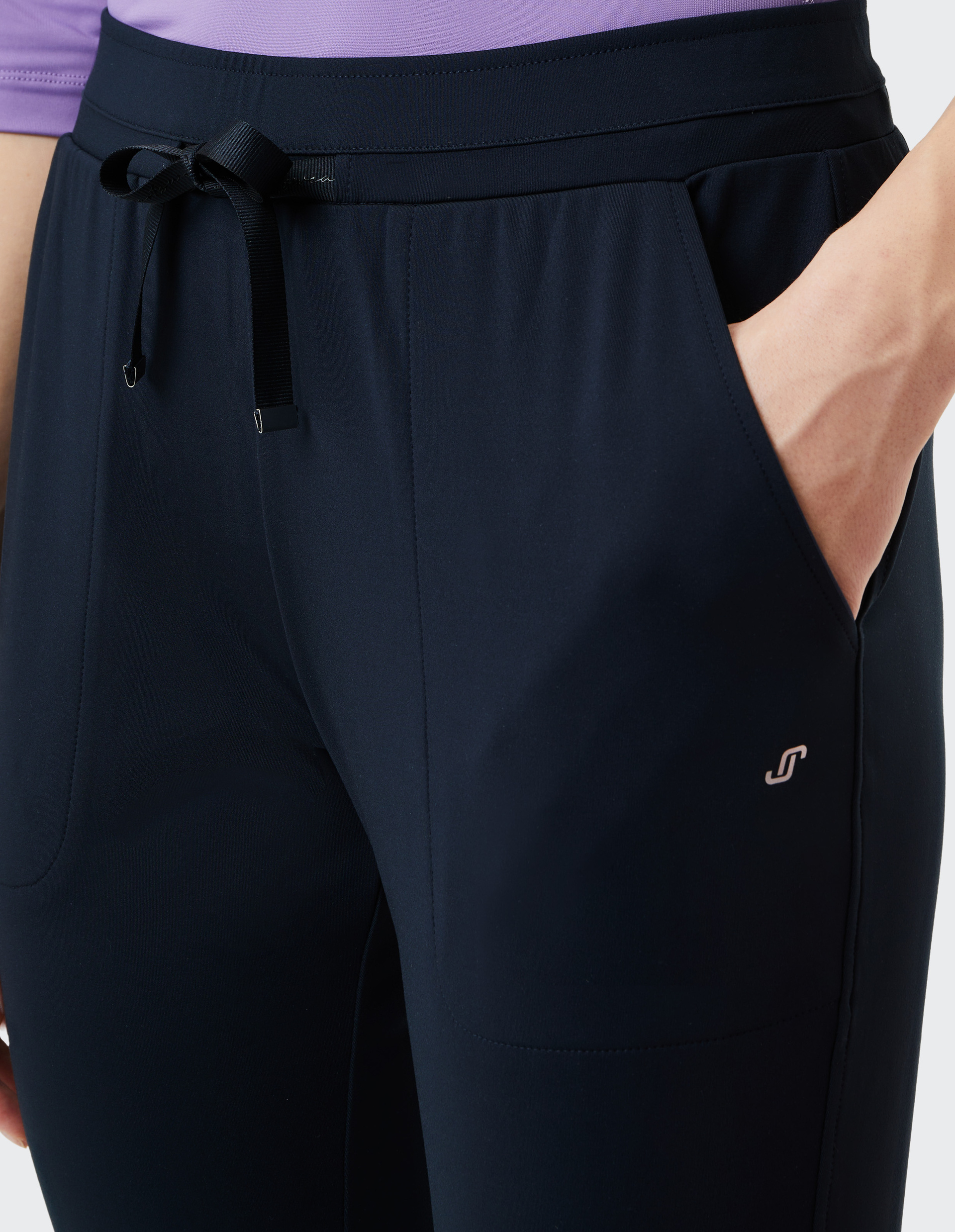 Dunkelblaue Sporthose mit Kordelzug am Bund und eingesteckter Hand in der rechten Tasche, kombiniert mit einem lila Oberteil.